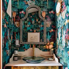 a bathroom with colorful wallpaper and a mirror on the sink area, surrounded by gold pedestals