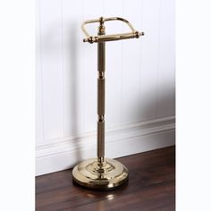 an antique brass plated toilet roll holder on a wooden floor with white walls in the background