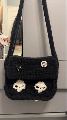 a black crocheted purse with eyes on the front hanging from a hook in a room