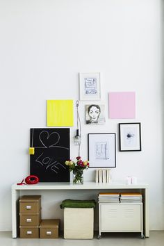 a white shelf topped with pictures and boxes next to a wall covered in art pieces