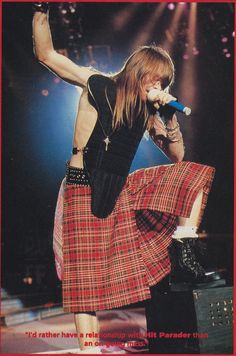 a woman with long hair wearing a skirt and holding a microphone in her hand while standing on stage