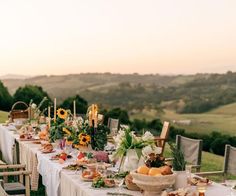 a long table is set up with food and candles for an outdoor dinner in the countryside