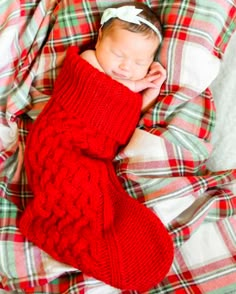 a baby wrapped up in a red sweater laying on top of a plaid bed spread