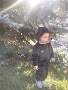 a small child in a bear suit standing next to a tree with sun shining on it