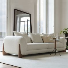 a white couch sitting in front of a window next to a table with a mirror on it