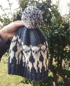 a hand holding a knitted hat in front of a tree