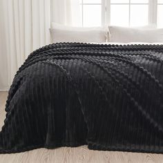 a bed with black bedspread and pillows in front of a white curtained window