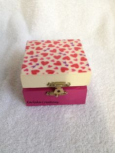 a pink and white box with hearts on it sitting on a bed next to a towel