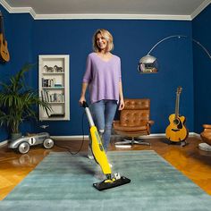 a woman is vacuuming the floor in her living room with blue walls and leather furniture