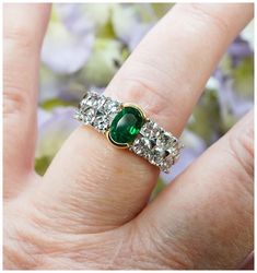 a close up of a person's hand with a ring on their finger and flowers in the background