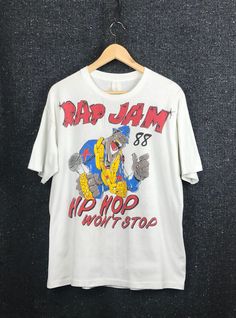 "Brand: Tag illegible Tag Size: N/A Fit:  (see measurements below) - Main Color: White  - Front: Graphic + \"Hip Hop Won't Stop\" + \"Rap Jam 88\" - Reverse: Artist graphics: Kool Moe Dee / Doug E Fresh / BDP / Big Daddy Kane + Erik B & Rakim - Sleeve: Short - Neckline: Crew - Stitching: Single - Fabric Composition: Uncertain - Origin Country: Uncertain Condition: Poor / Vintage - 1988 - Staining / flaws - Pit stains  - Run in fabric near neckline APPROXIMATE MEASUREMENTS - Pit-Pit: 21.5\" - Shoulder Seam Width:  22\" - Sleeve: 18.75\" - Length: 27\"" Vintage Fitted Tops With Logo Print, Fitted Vintage Tops With Logo Print, Throwback White Tops For Streetwear, Retro Cotton Tops For Streetwear, Throwback Cotton Top For Streetwear, Summer Streetwear Tops With Vintage Print, Vintage Print Tops For Summer Streetwear, Retro White Top With Letter Print, Throwback Cotton T-shirt For Streetwear