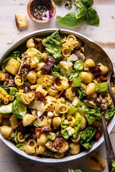 a bowl full of pasta salad with spinach, bacon and lettuce on the side