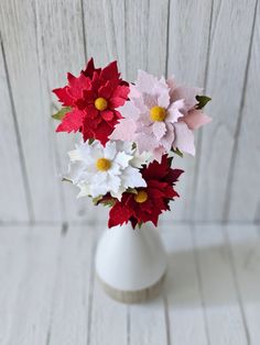 a white vase filled with red, white and pink flowers on top of a wooden table