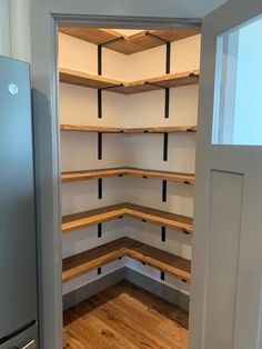 an empty pantry with wooden shelves and stainless steel refrigerator in the corner between two walls