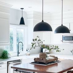 an island in the middle of a kitchen with stools and lights hanging over it