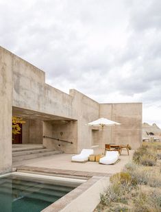 an outdoor patio with chairs and umbrellas next to a swimming pool in the desert