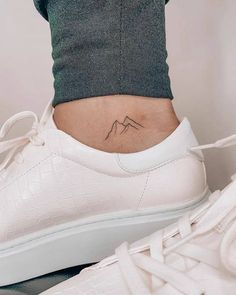 a woman's foot with a small mountain tattoo on the side of her ankle