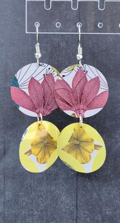 two yellow and pink flower earrings hanging from hooks on a gray surface with an acrylic sign in the background