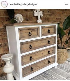 a white and brown dresser sitting on top of a floor next to a brick wall