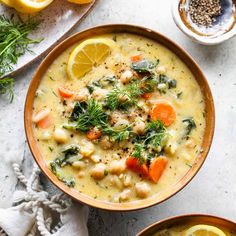 two bowls filled with soup and garnished with lemons, carrots and herbs