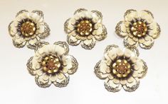 four white and gold flower brooches sitting next to each other