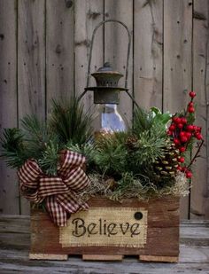 a wooden box filled with evergreens and pine cones on top of a table next to a lantern