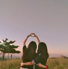 two women standing in the middle of a field making a heart shape with their hands