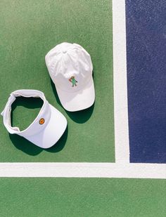 two white hats sitting on top of a tennis court next to a blue and green wall