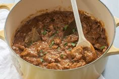 a pot full of stew with a wooden spoon in it on a white table cloth