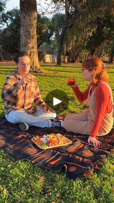 a man and woman sitting on a blanket in the grass eating food from a plate