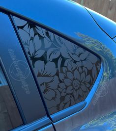 the side window of a blue car with flowers on it's decal, in front of a wooden fence