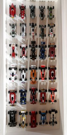 a collection of toy cars on display in a white box with shadow from the wall