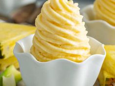 two white bowls filled with food on top of a wooden table next to pineapples