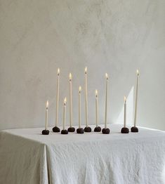 seven candles lined up on a table with white linen draped around them and one candle lit in the middle