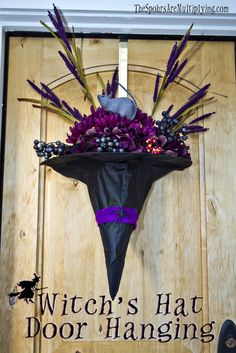 a fake witch's hat hanging on a door with purple flowers and feathers in it