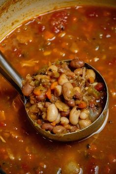 a ladle full of beans and vegetables is being stirred by a spoon in a pot