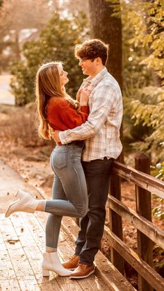 a man and woman standing on a bridge in the woods with their arms around each other