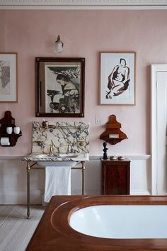 a bathroom with pink walls and pictures on the wall above the bathtub is shown