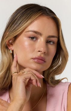 a woman with blonde hair wearing a pink top and gold jewelry, looking at the camera