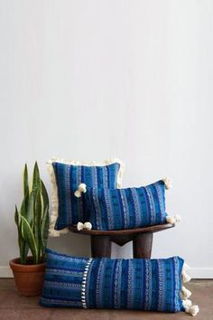 three blue and white striped pillows sitting on top of a wooden table next to a potted plant