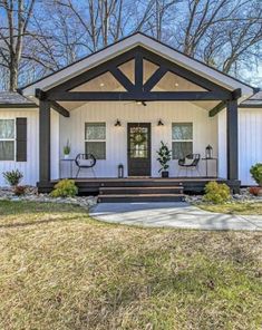 a white house with black trim on the front porch and two chairs sitting outside it