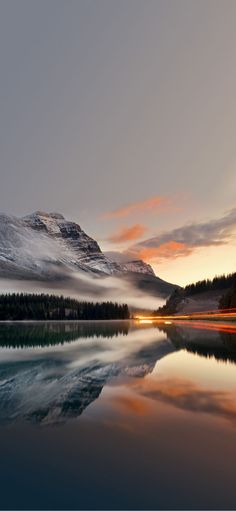 the sun is setting over a mountain range with water and trees in front of it