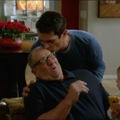 an older man is hugging a young boy in the living room while another child looks on