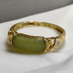 10K Yellow Gold and Jade Vintage Ring Embrace the allure of timeless elegance with this exquisite 10K Yellow Gold and Jade Vintage Ring. This classic piece features a beautifully polished jade stone, known for its serene green hue and symbolic meanings of purity and harmony. The jade is gracefully set within a 10K yellow gold band, which enhances its natural beauty and creates a striking contrast that draws the eye. Adding to its charm, the ring showcases a delicate crossover design on each side, adorned with a small, sparkling diamond accent, offering a subtle touch of brilliance. The vintage design of this ring makes it a unique and meaningful accessory, perfect for those who appreciate both beauty and history. Whether worn as a statement piece, a special gift, or a meaningful addition t Jade Engagement Ring Gold, Green Diamond Ring Engagement, Vintage Jade Ring, Jade Gold Ring, Vintage Engagement Rings Green, Gold Engagement Rings Indian, Green And Gold Ring, Jade Wedding Ring, Etsy Jewelry Rings