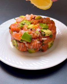 a person is holding up a piece of salmon on a plate with cucumbers and lemon wedges