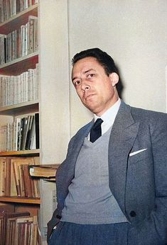 a man in a suit standing next to a bookshelf