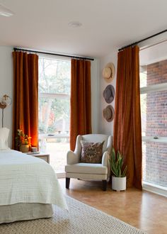 a bedroom with orange drapes and a white chair in front of the window,