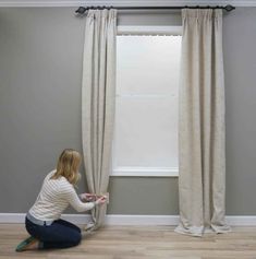 a woman is sitting on the floor in front of a window with curtains and blinds