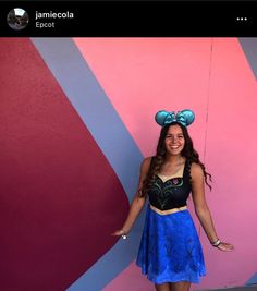 a woman standing in front of a pink and blue wall with minnie mouse ears on her head