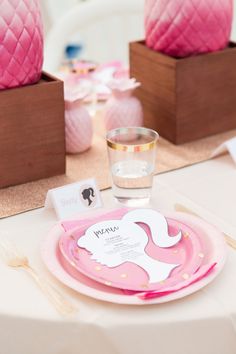 a pink and gold table setting with plates, napkins, cups and vases